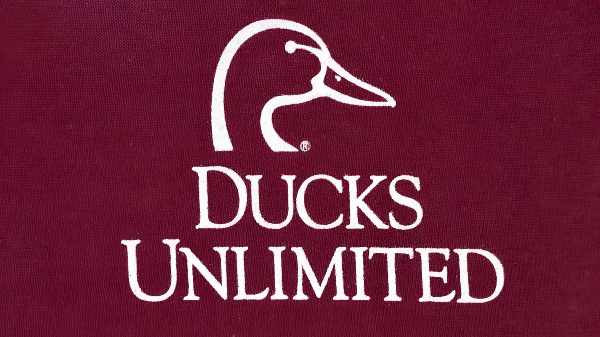  壁紙 — 一個清晰的白色 Ducks Unlimited 標誌，帶有風格化的鴨頭和粗體文字，在帶有紋理的栗色布料背景上脫穎而出。