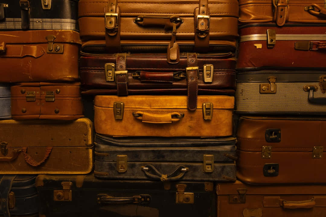  壁紙 — 堆疊的復古皮革行李箱，溫暖的棕色和褪色的藍色在柔和燈光下閃耀。