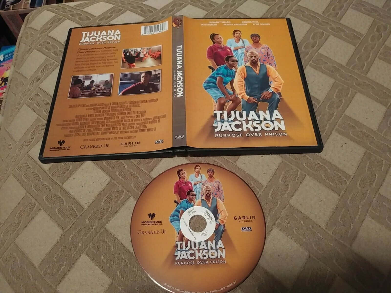 Celebrity 桌布 壁紙 — 《Tijuana Jackson》的DVD盒和光碟打開放在有圖案的布料表面上，展示電影藝術作品和製作人員名單。