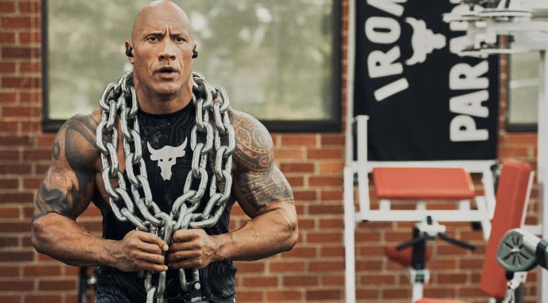 Project Rock 桌布 壁紙 — Dwayne Johnson 在粗糙的磚牆健身房中，脖子上掛著沉重的鐵鍊用力。
