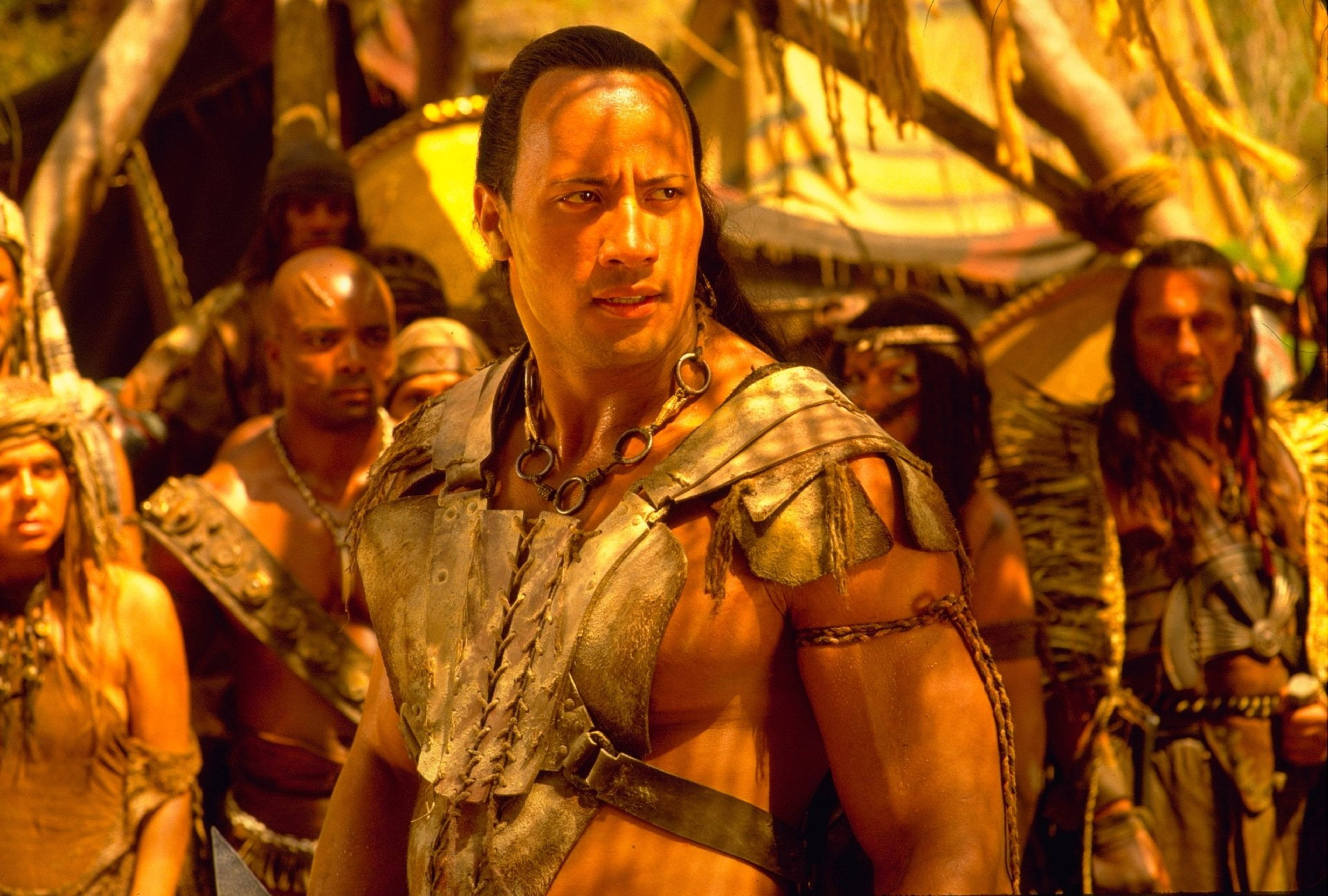 Dwayne 桌布 壁紙 — Dwayne Johnson 飾演一位肌肉發達的戰士，身穿部落盔甲，站在畫面中央，周圍是叢林環境中的其他戰士。