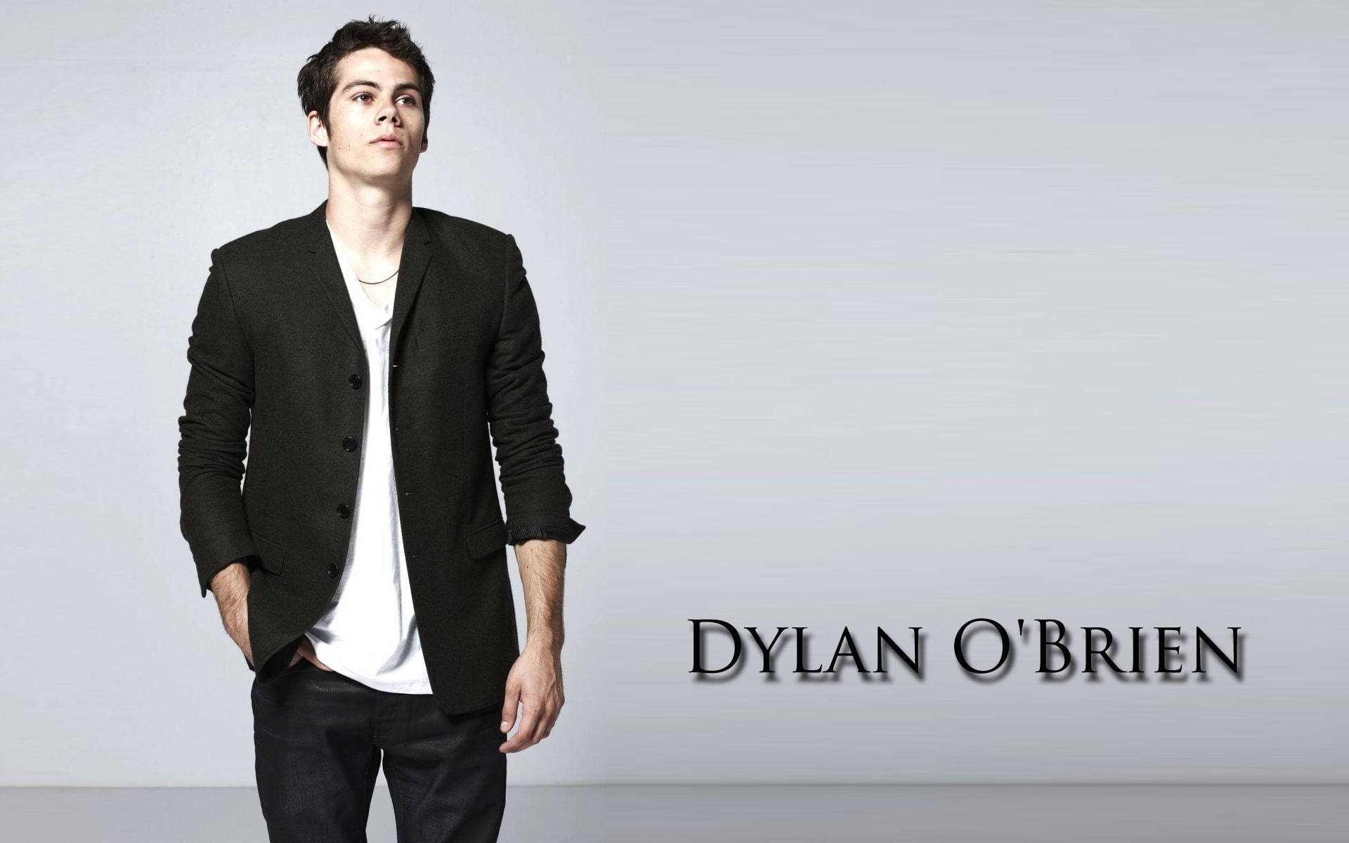 dylan 桌布 壁紙 — Dylan O'Brien 自信地站在簡約灰色工作室背景前，身穿黑色西裝外套和白色T恤。