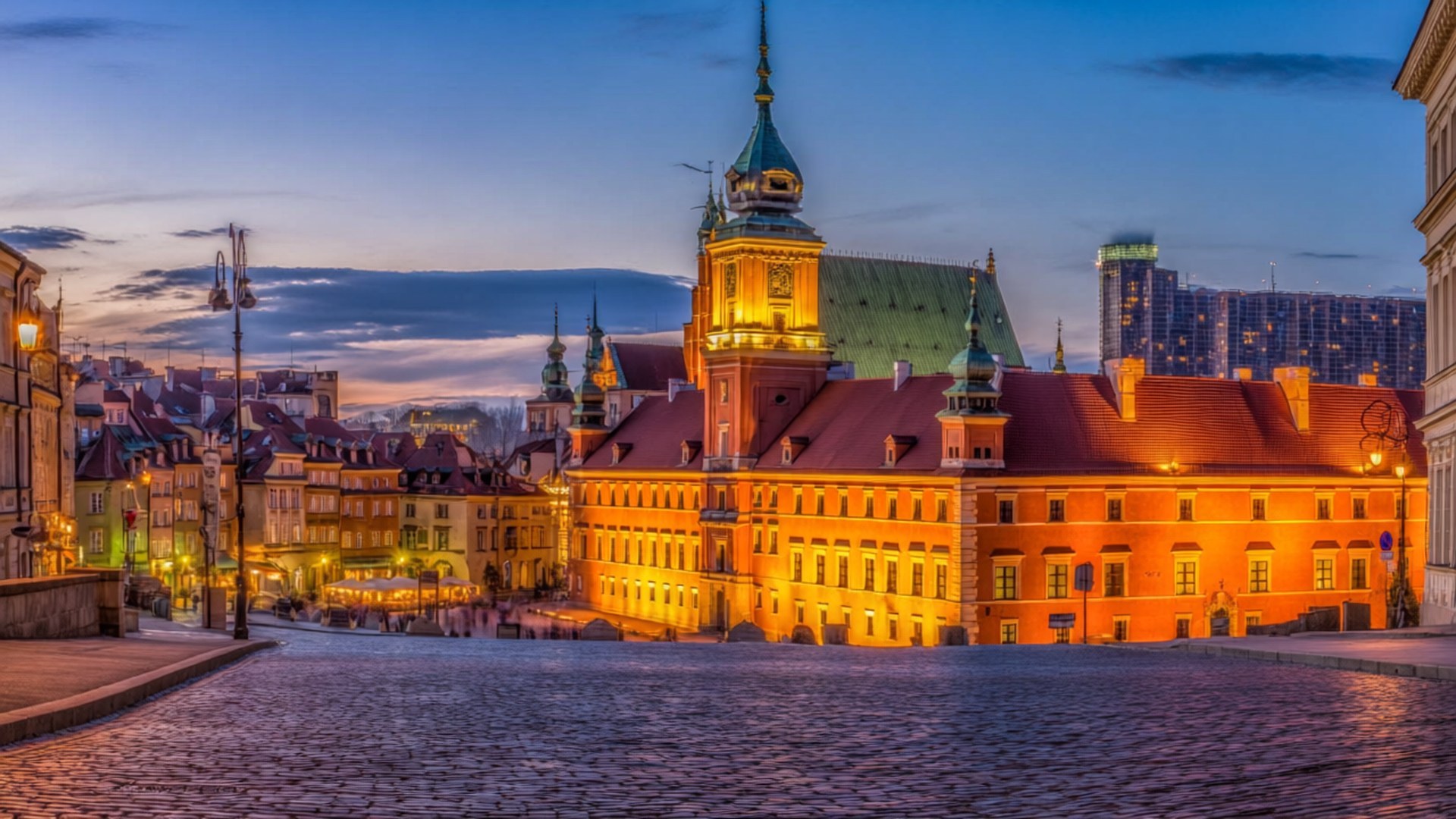Warsaw Old Town Dusk 壁紙 — 一條鵝卵石街道通向一座宏偉的燈光城堡，擁有紅色屋頂和綠色尖塔，在暮色天空下。
