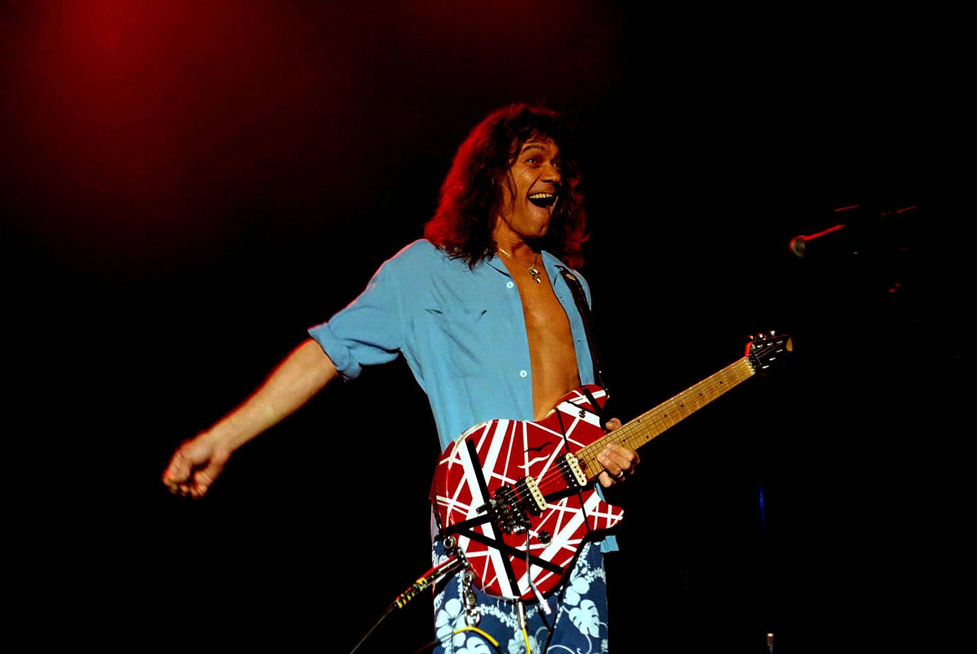 Eddie 桌布 壁紙 — Eddie Van Halen 在紅色燈光下於舞台上張開雙臂，帶著喜悅的表情彈奏吉他。