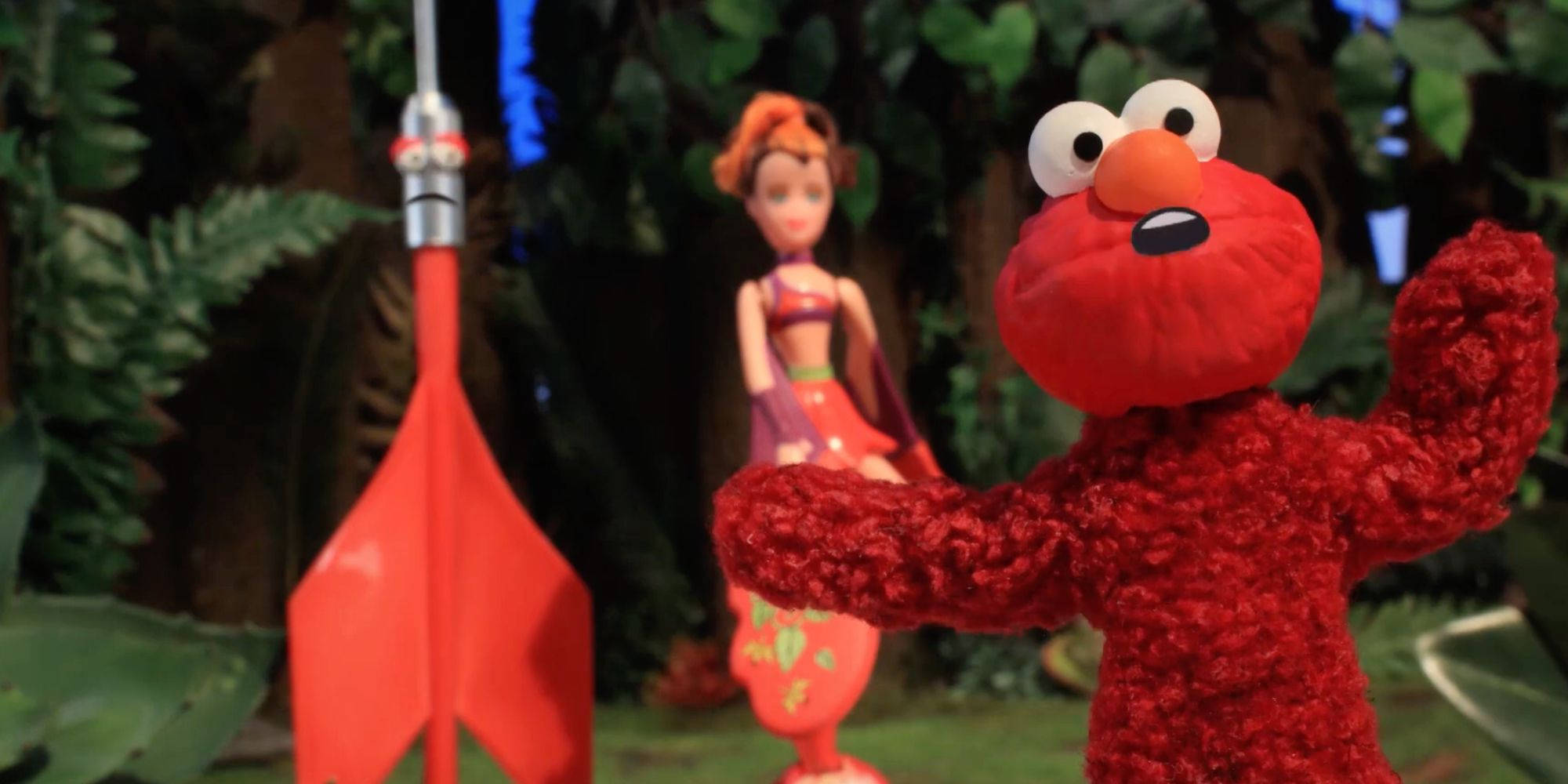 Animated 桌布 壁紙 — Elmo 在叢林場景中站在紅色火箭前面，手裡拿著一個娃娃。