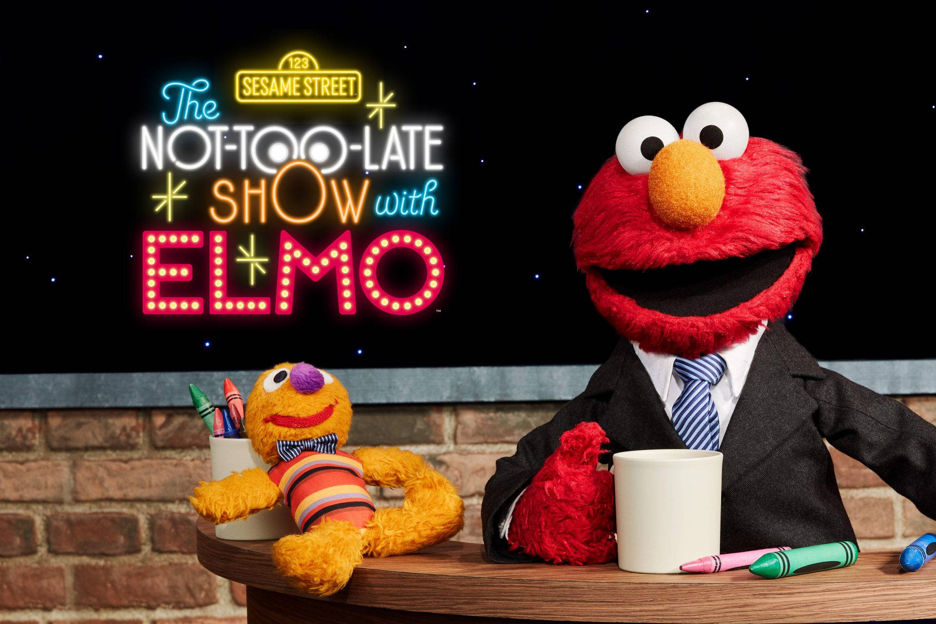 Elmo 桌布 壁紙 — Elmo 身穿西裝主持深夜節目，背後有霓虹燈牌，磚牆佈景中有一位黃色木偶嘉賓。