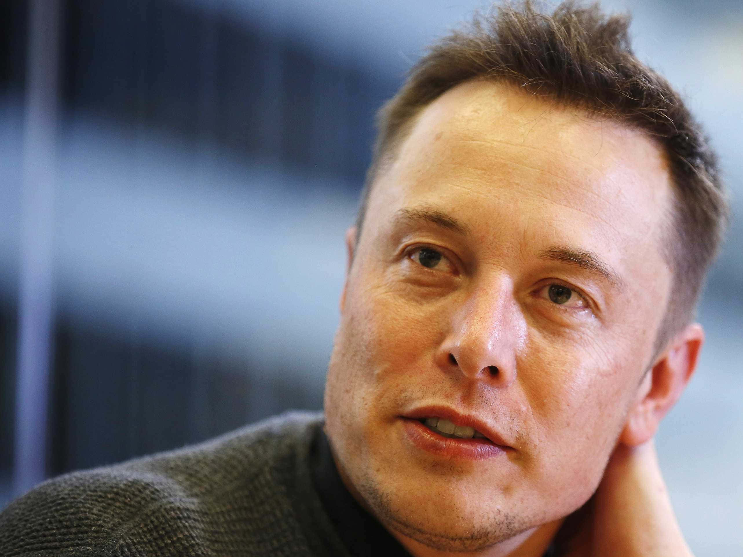 伊隆·馬斯克 桌布 壁紙 — Elon Musk 的特寫肖像，他手放在脖子附近，若有所思地望著模糊的現代背景。