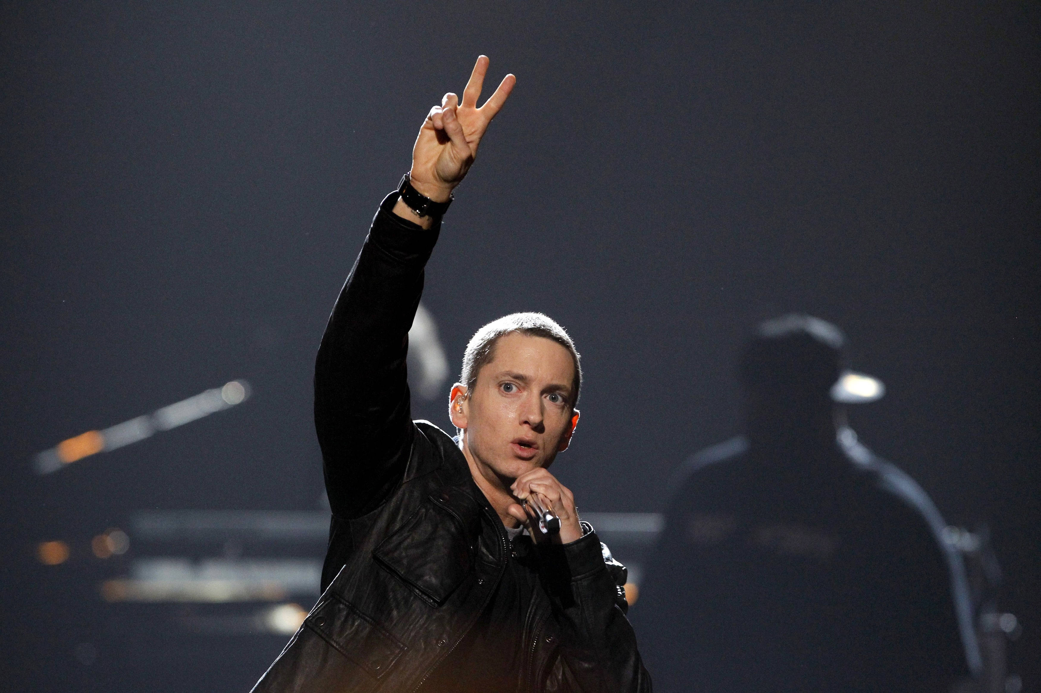 阿姆 桌布 壁紙 — Eminem 在舞台上手持麥克風，在戲劇性的舞台燈光下舉起和平手勢表演。