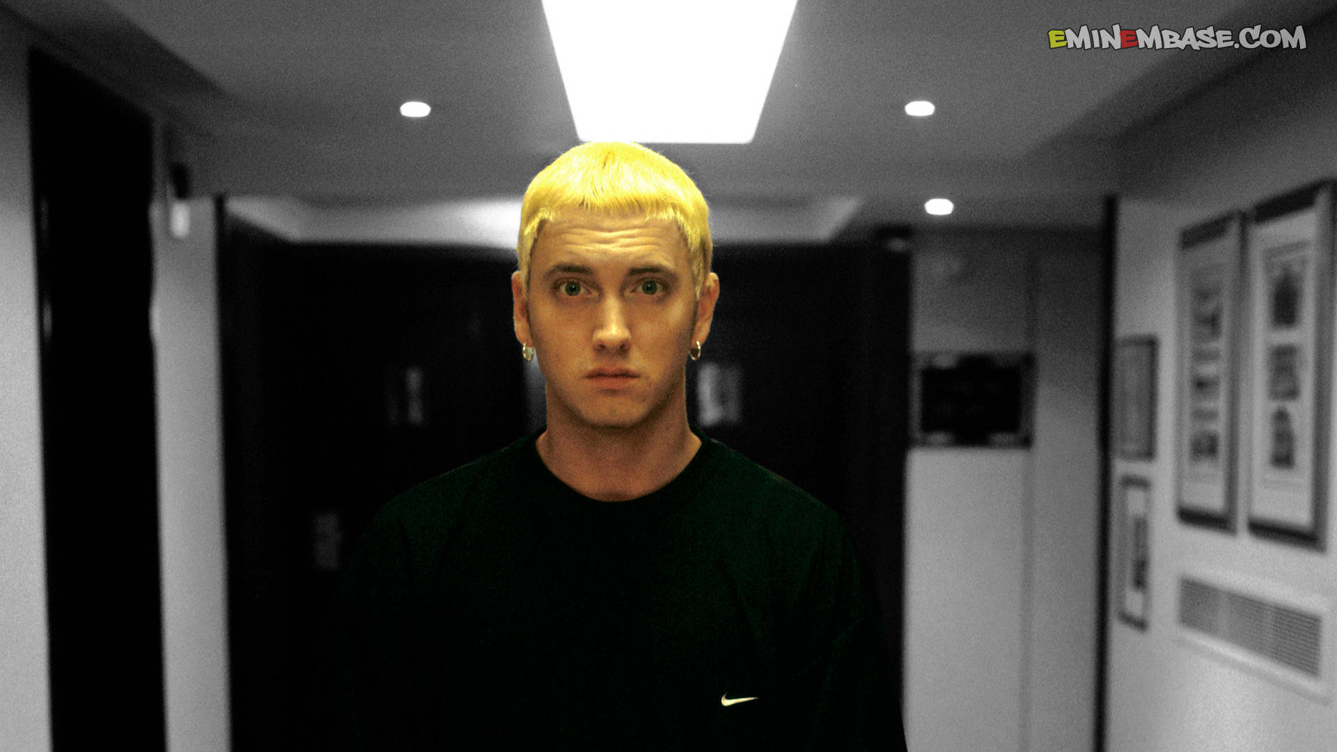 阿姆 桌布 壁紙 — Eminem 沿著一條燈光昏暗的飯店走廊，頭頂有強烈的螢光燈，凝視著前方。