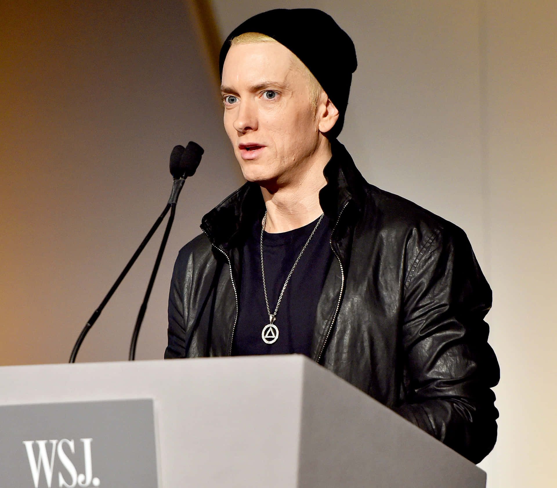 阿姆 桌布 壁紙 — Eminem 站在WSJ講台上，身穿黑色毛帽皮夾克和銀色吊墜，對著麥克風講話。