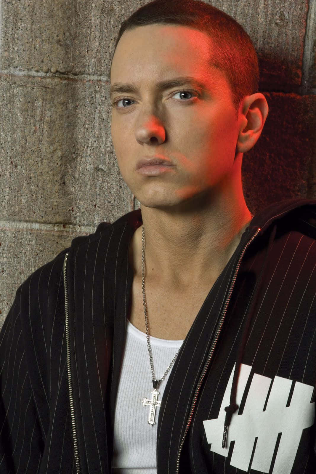 阿姆 桌布 壁紙 — Eminem 靠在混凝土牆上，在戲劇性的紅光下，穿著條紋連帽衫和十字架項鍊。