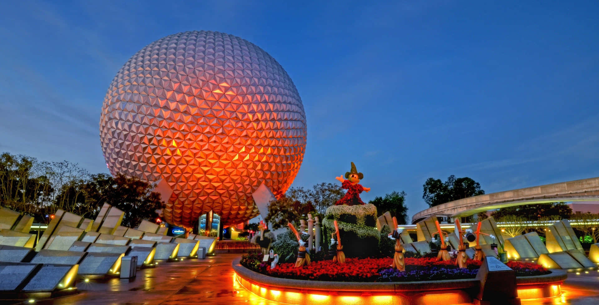 迪士尼世界 桌布 壁紙 — Epcot 標誌性的測地線球體在暮色天空下溫暖地發光，周圍環繞著充滿活力的花卉展示和照明小徑。