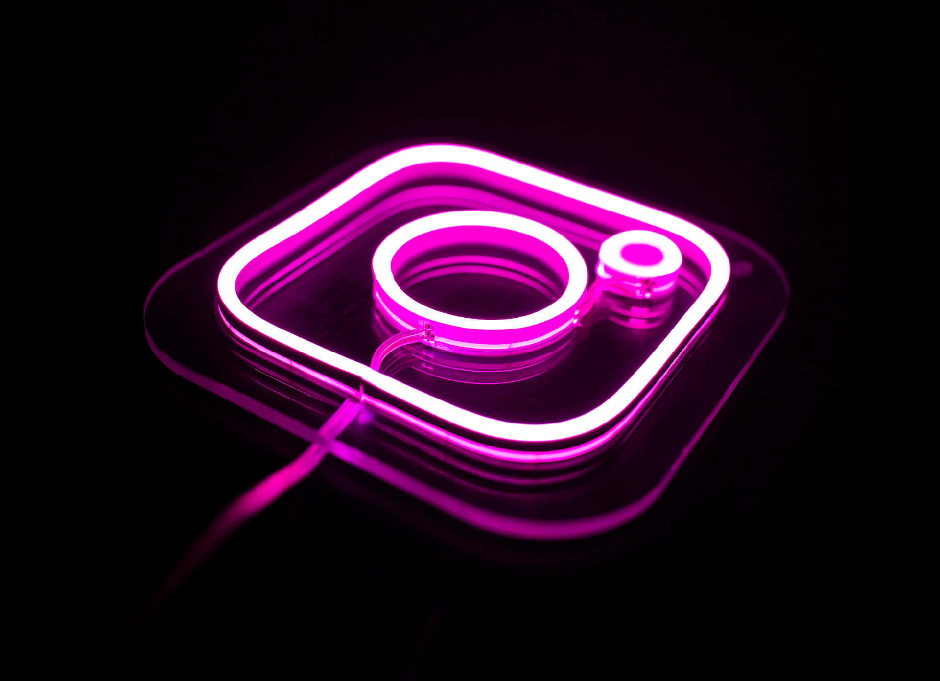 在深色反光表面上發光的粉紅色霓虹燈Instagram標誌。 — Instagram 壁紙