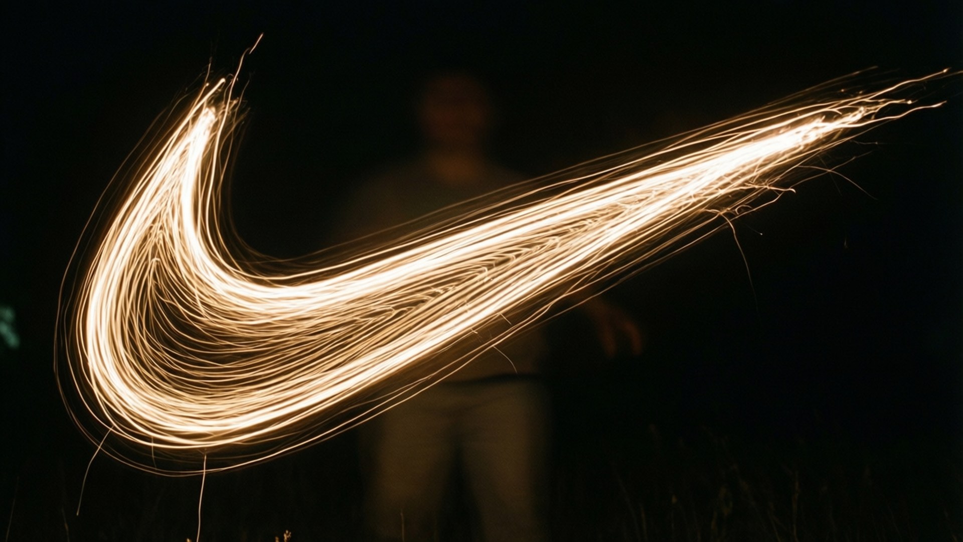 Light Trail Swoosh 壁紙 — 一個發光的金色Nike勾勾，由光軌形成，以黑暗夜空為背景，背後有一個模糊的人影。