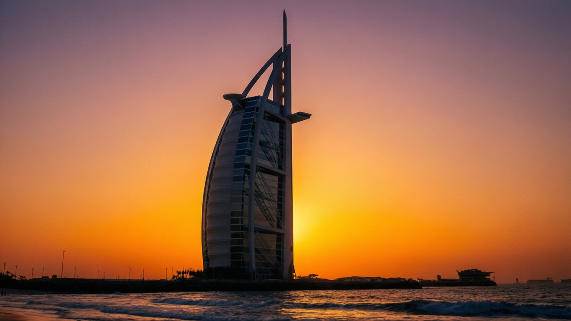 Burj Al Arab Golden Hour 壁紙 — 帆船酒店以流線型帆船剪影矗立在海洋上空充滿活力的橙色和紫色日落天空下。