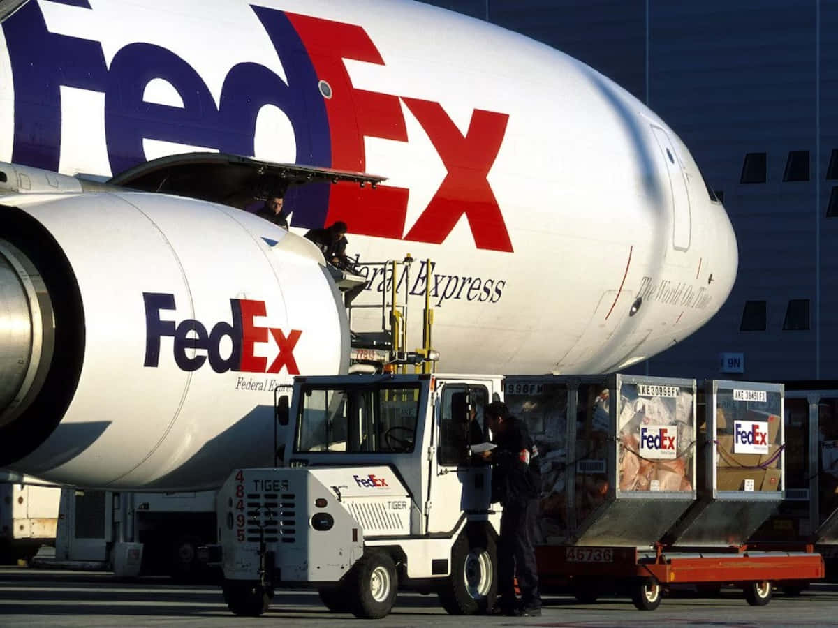 聯邦快遞 桌布 壁紙 — FedEx貨機在明亮的日光下，由工人使用品牌卡車在機場停機坪裝載貨物。