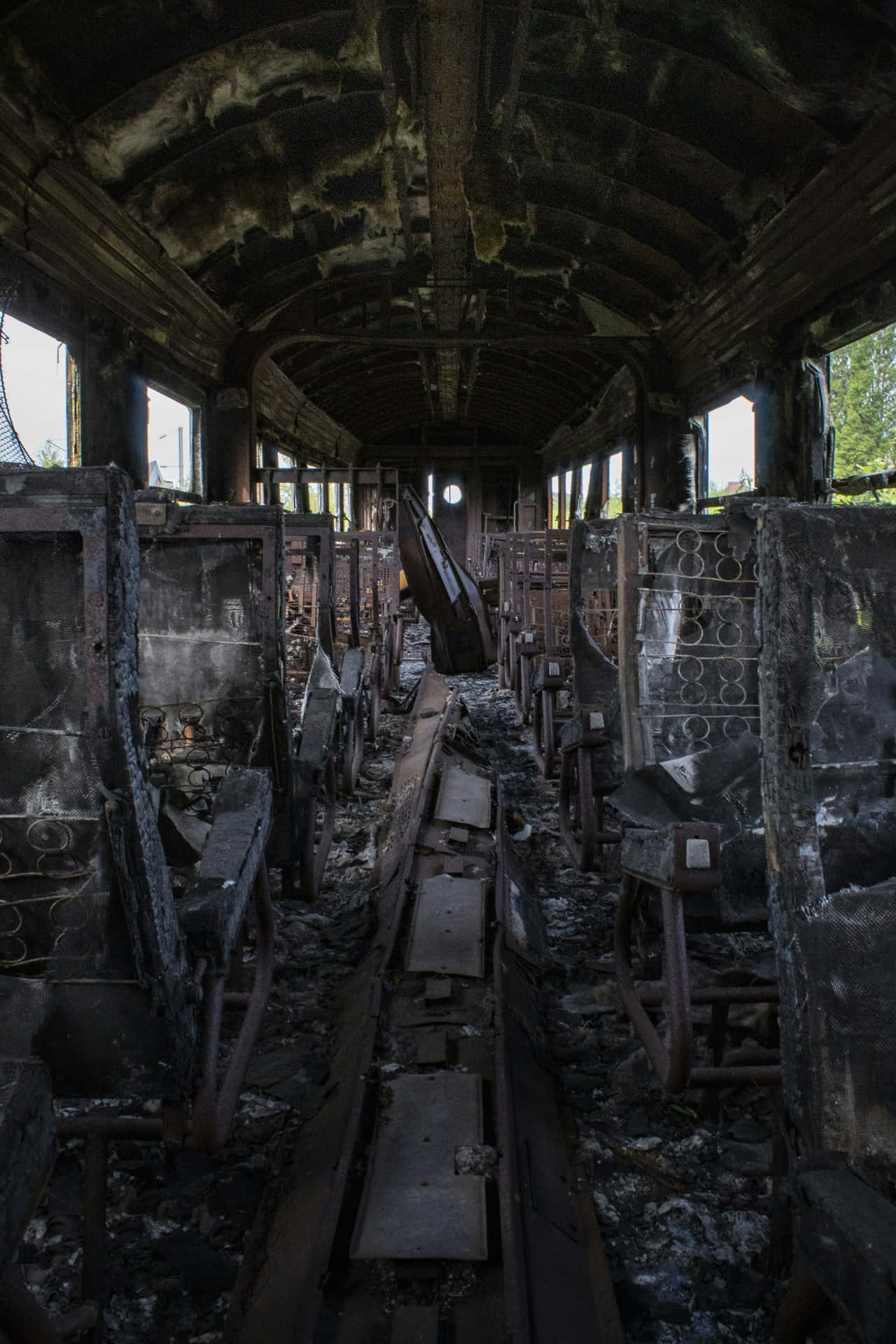  壁紙 — 廢棄火車車廂內部被燒焦，破爛座椅和瓦礫在透過破碎車窗的昏暗自然光下顯露出來。