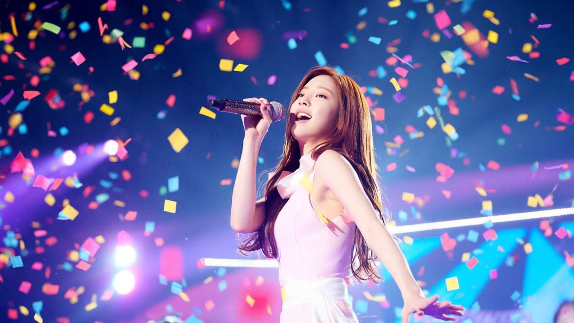 Concert Confetti Taeyeon 壁紙 — 一位身穿白色連衣裙的女歌手在充滿活力的舞台燈光下，熱情地對著麥克風演唱，五彩紙屑如雨般落下。