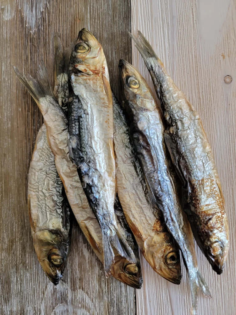  壁紙 — 五條乾燥的沙丁魚，帶有皺紋的銀色魚皮，放在風化的木質表面上。