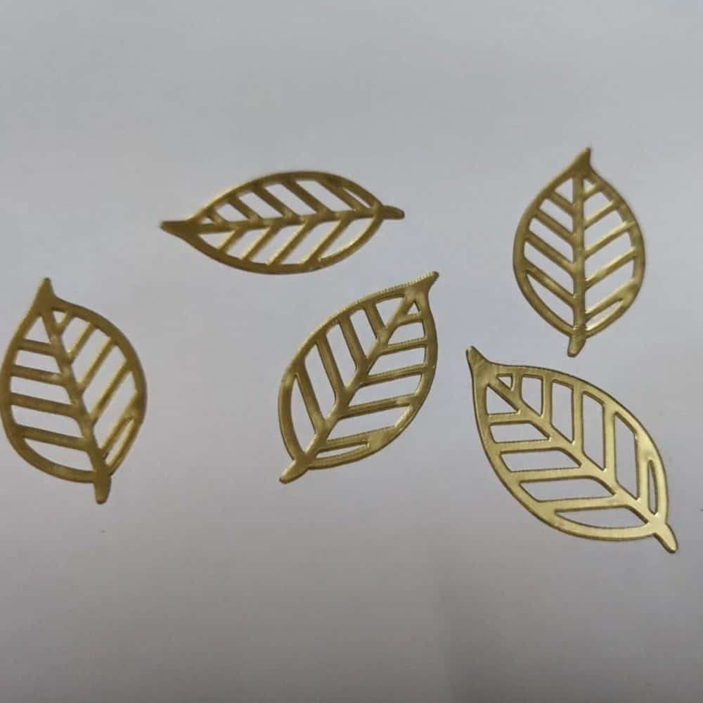  壁紙 — 五個金色葉形鏤空剪紙，帶有葉脈圖案，排列在純白表面上。