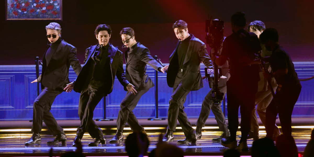 身穿黑色西裝的男舞者在燈光舞台表演，前景有觀眾。 — Bts 壁紙