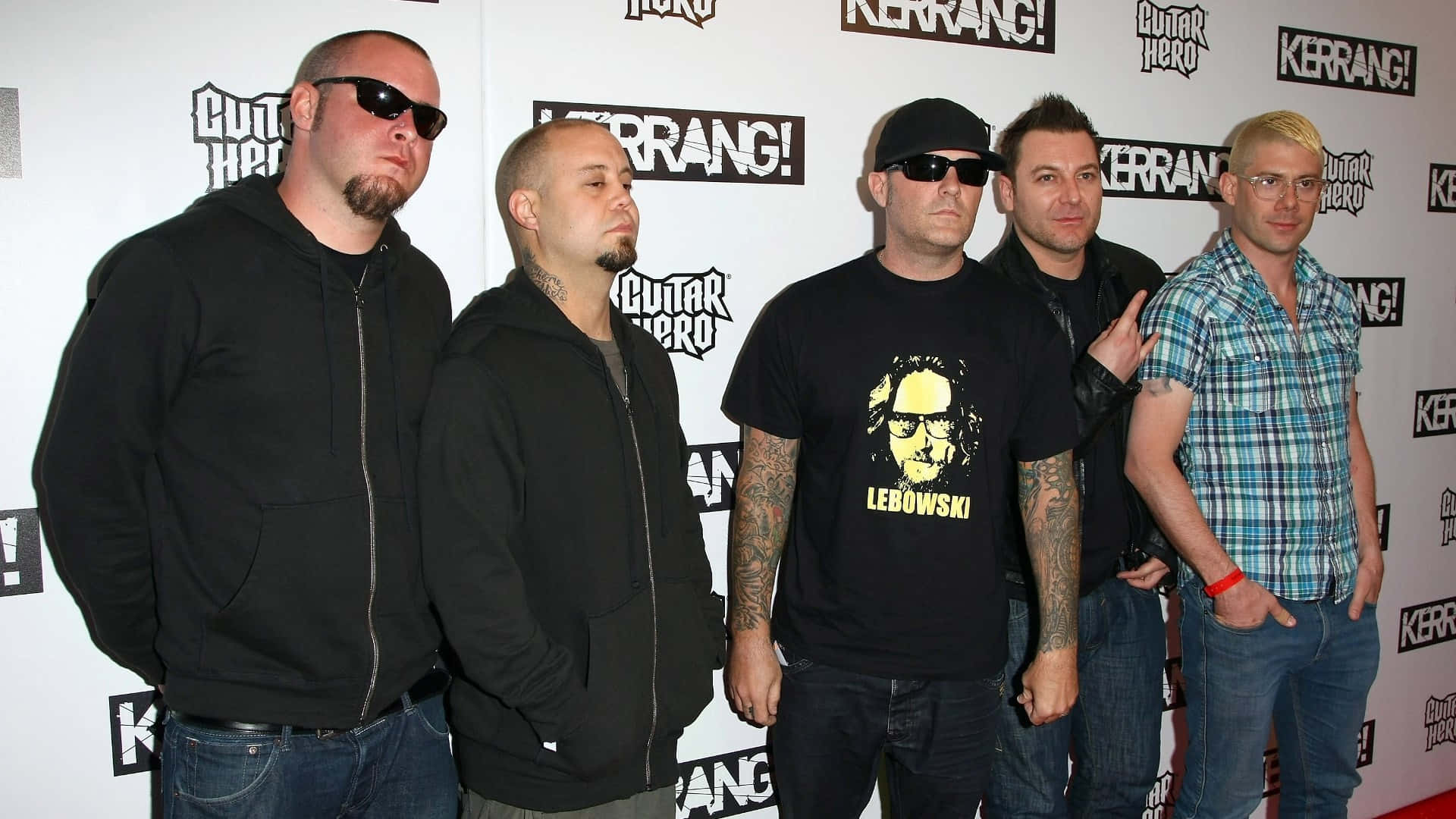  壁紙 — 五位身穿休閒服裝的男士在印有Guitar Hero和Kerrang標誌的品牌活動背景前自信地擺姿勢。
