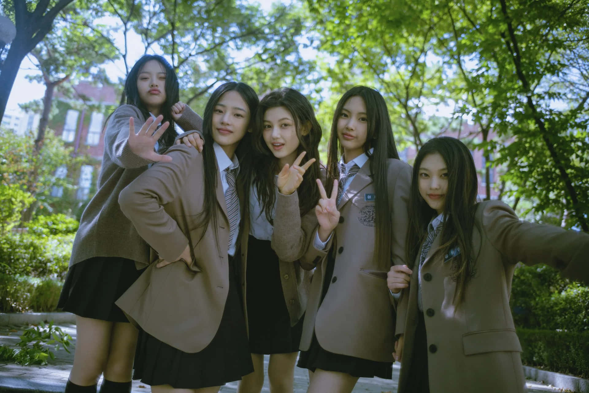  壁紙 — 五名身穿米色西裝外套和黑色裙子的女學生在明亮的綠樹下愉快地擺出和平手勢。