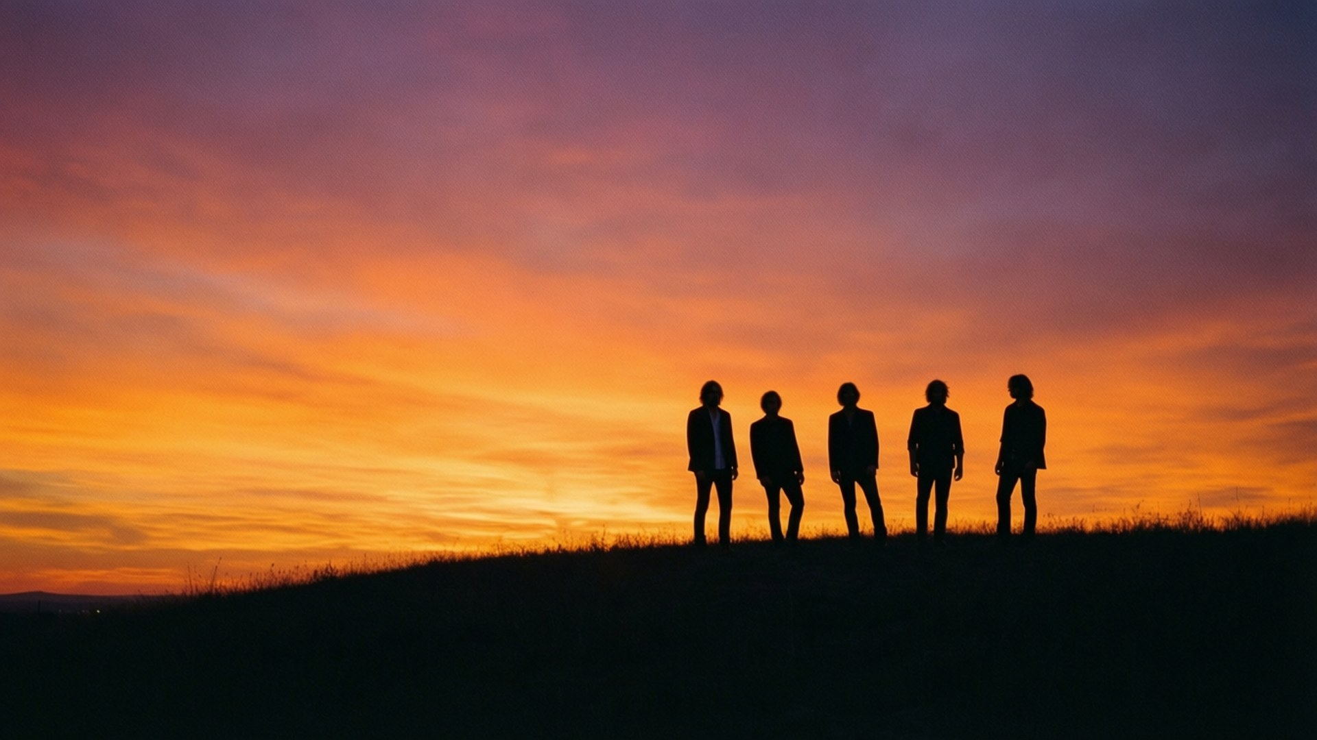 Sunset Silhouette 壁紙 — 五個剪影人物排成一排，站在長滿草的山丘上，背景是充滿活力的橙、紫、粉紅色的日落天空。
