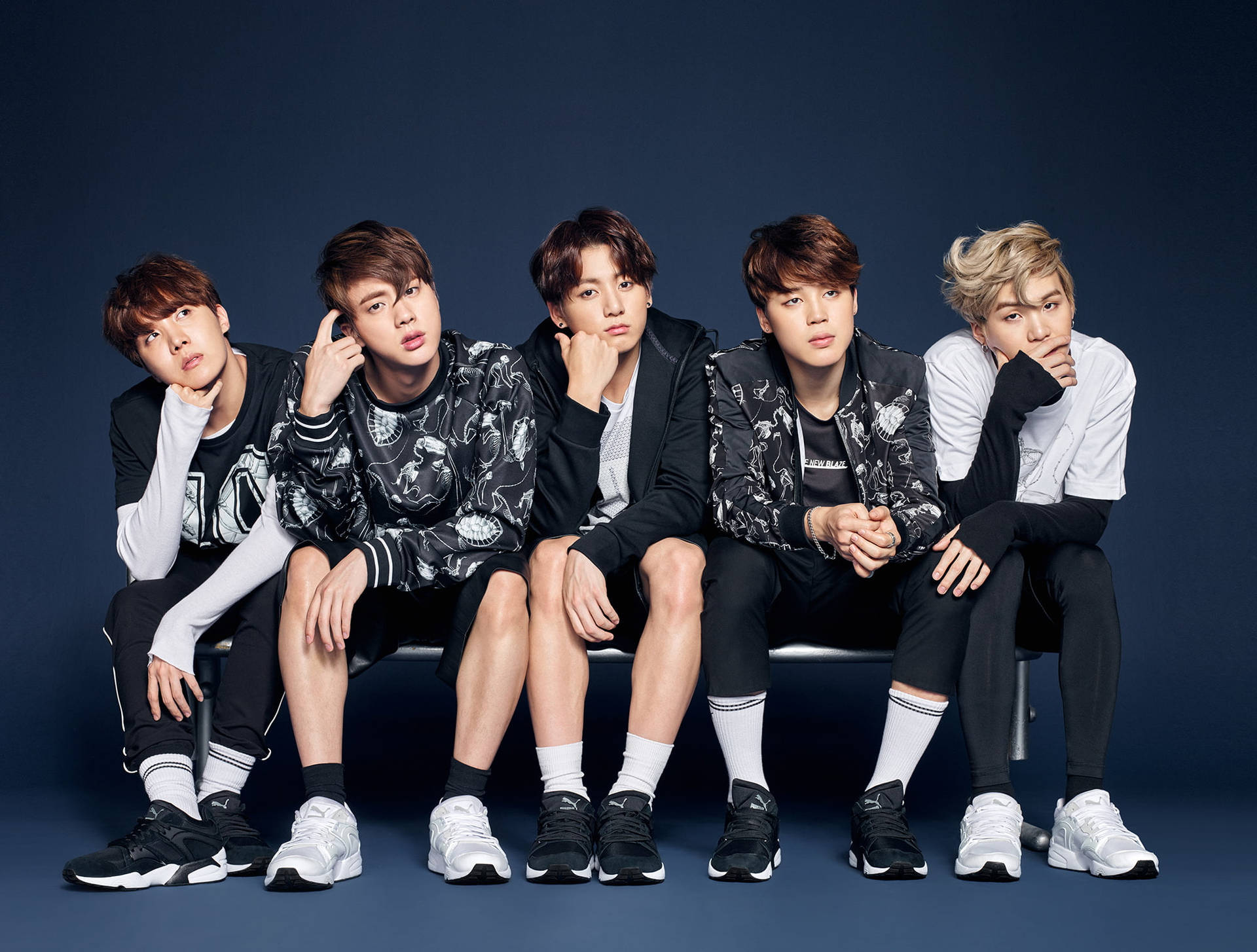 五位身穿時尚黑白服裝的年輕男士在攝影棚的長椅上擺姿勢。 — Jungkook 壁紙