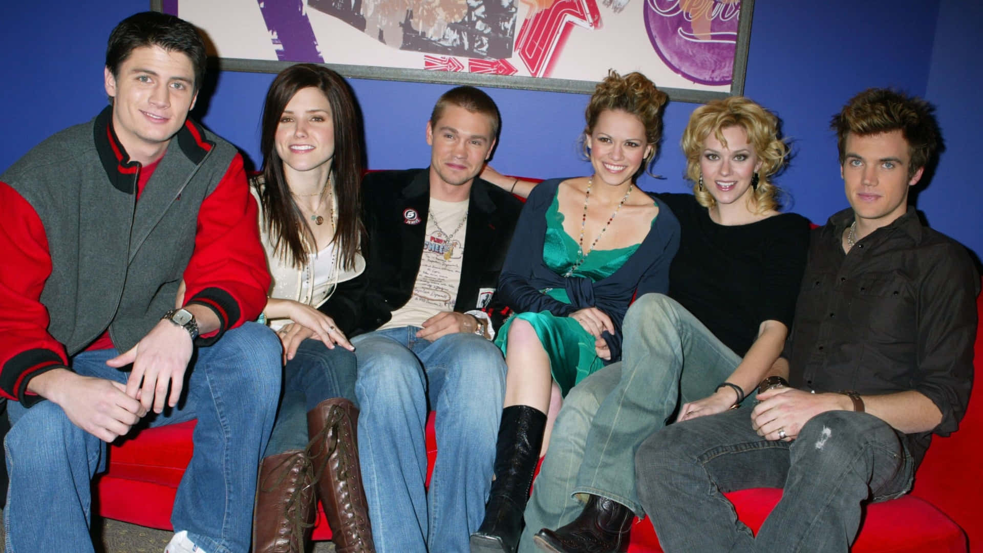  壁紙 — 來自《The O.C.》的五位年輕演員坐在紅色沙發上，背後是藍色牆壁和裱框藝術品，對著鏡頭微笑。