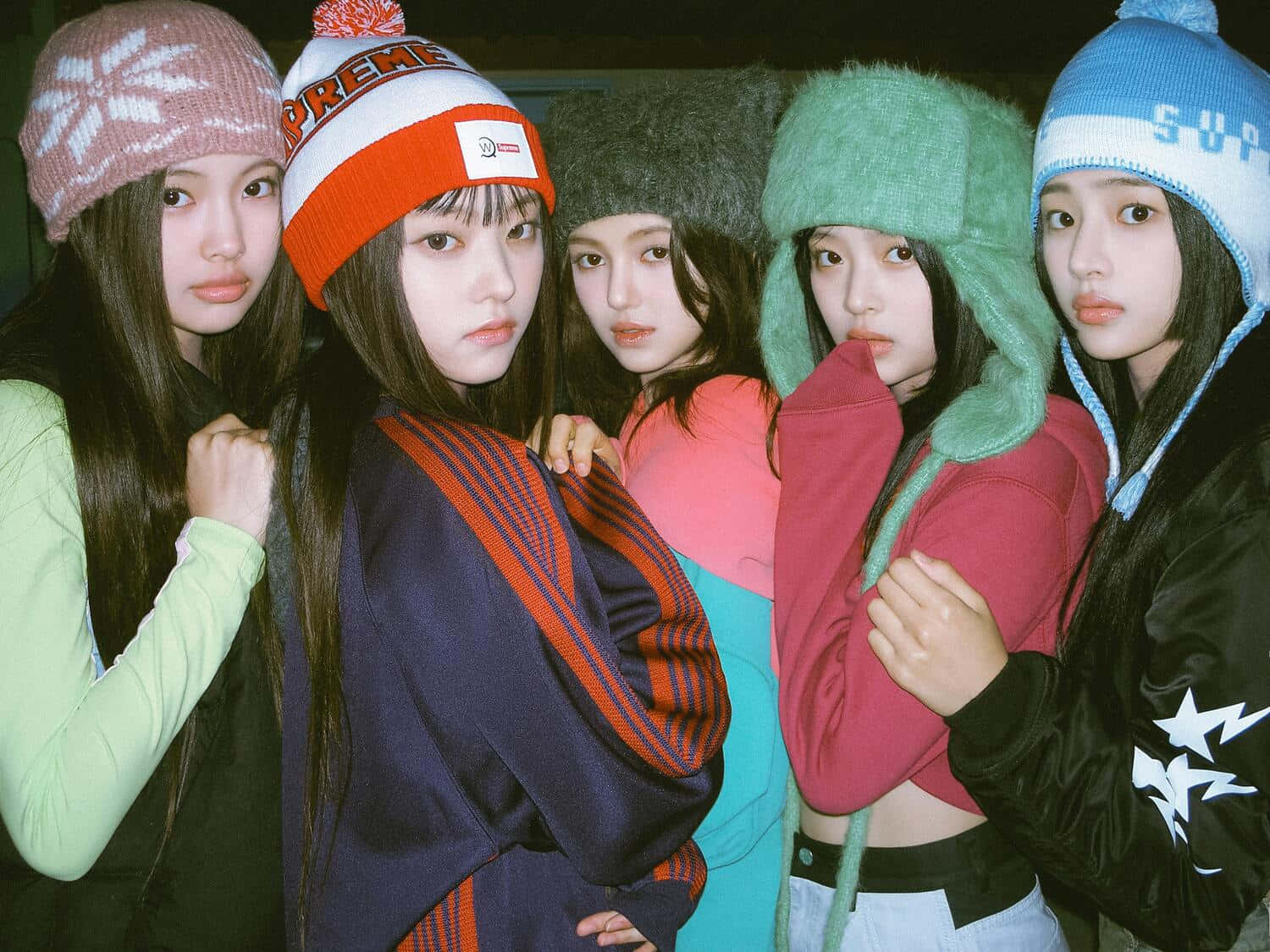  壁紙 — 五位年輕女性戴著色彩繽紛的冬季毛帽和舒適的衣服，緊密地站在一起，表情嚴肅。