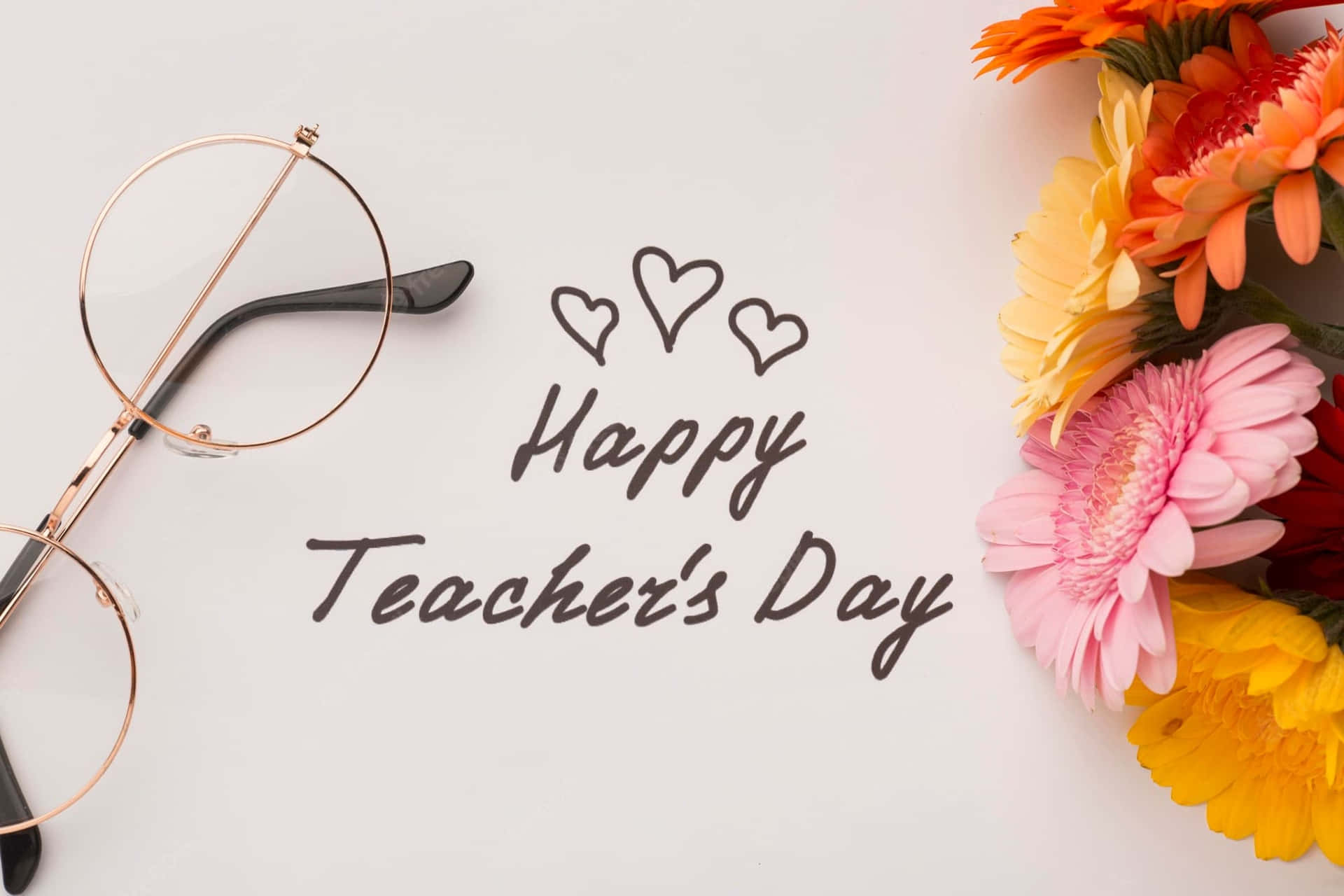 壁紙 — 玫瑰金眼鏡、手寫Happy Teacher's Day文字配愛心、白色背景上鮮豔的非洲菊雛菊花束的平鋪擺放。