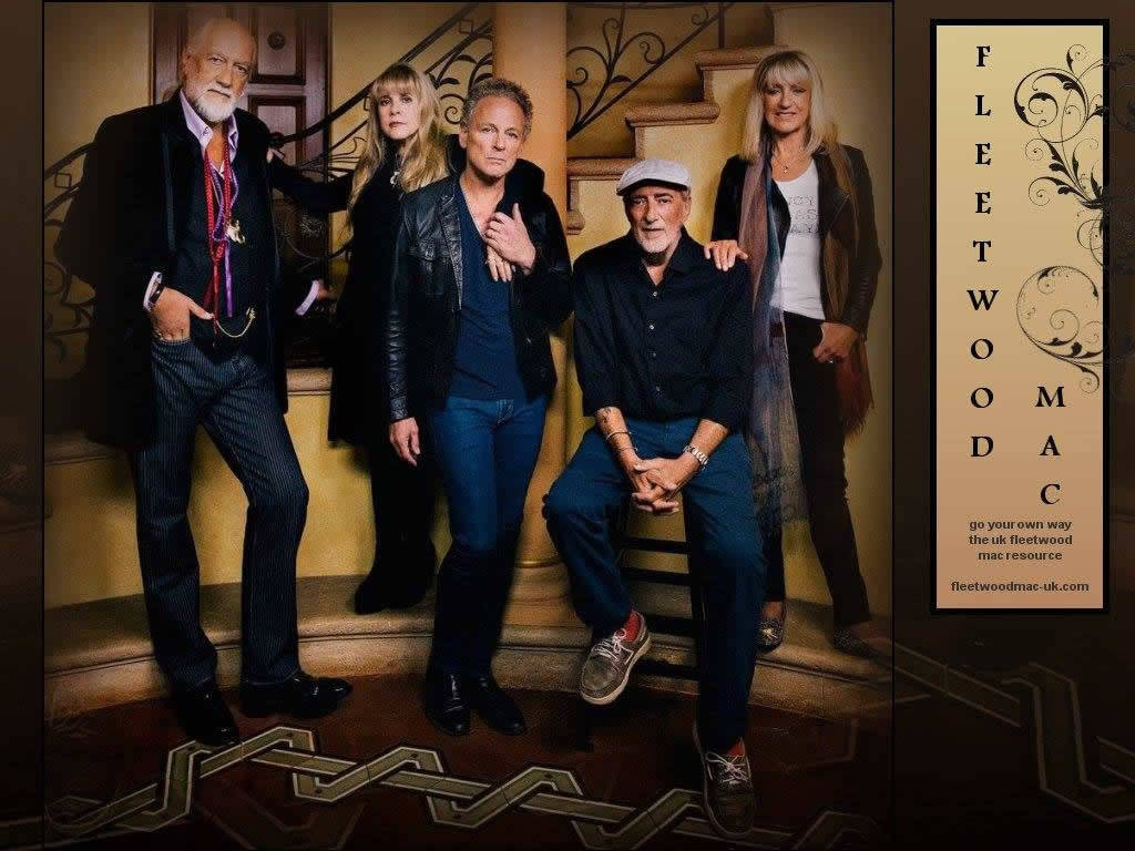 band 桌布 壁紙 — Fleetwood Mac 樂隊成員在溫暖燈光的復古室內環境中，自信地站在裝飾華麗的樓梯上，樓梯有裝飾欄杆和圖案地板。