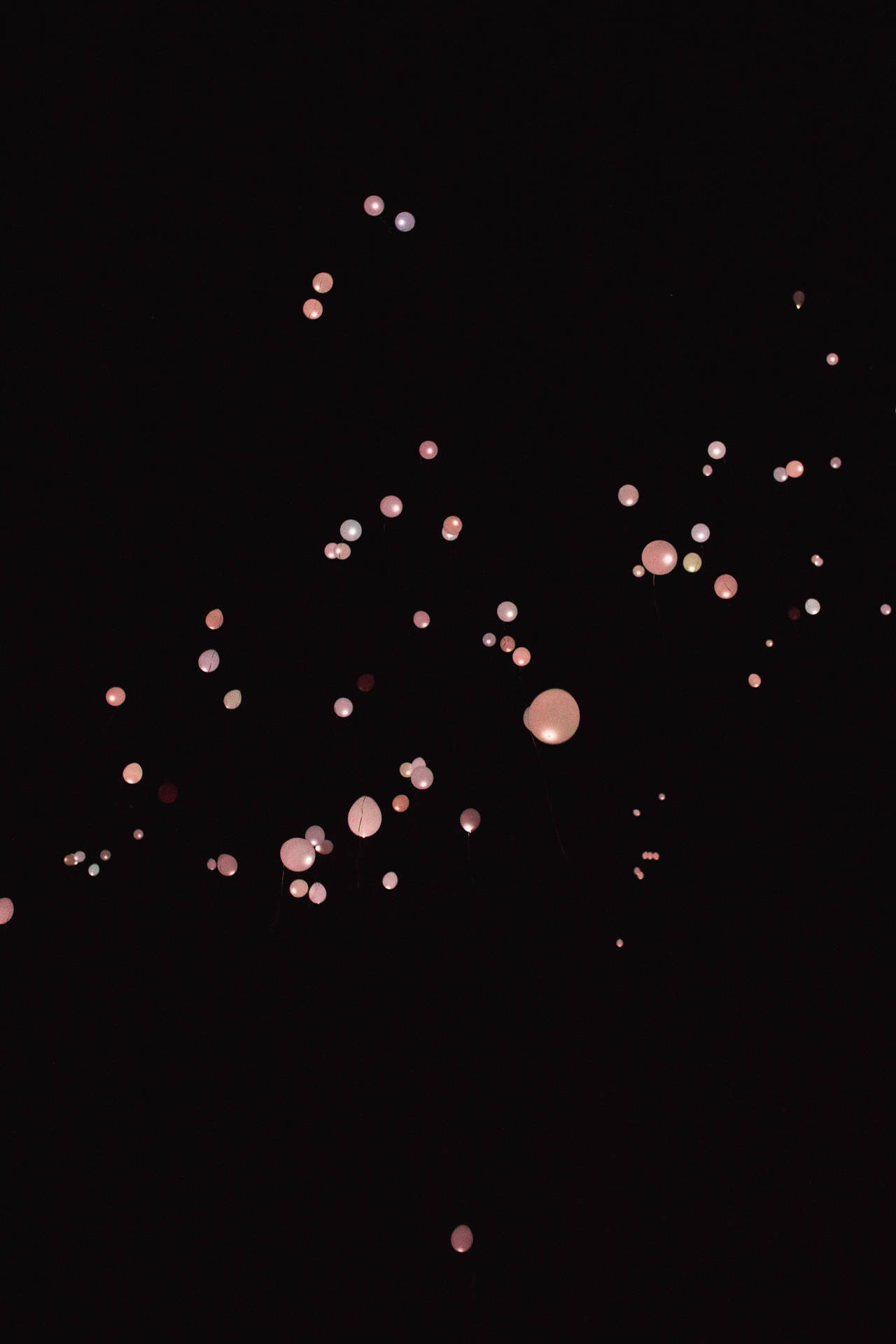 粉紅色和白色氣球在漆黑的夜空中飄浮。 — iPhone 13 Pro Max 壁紙