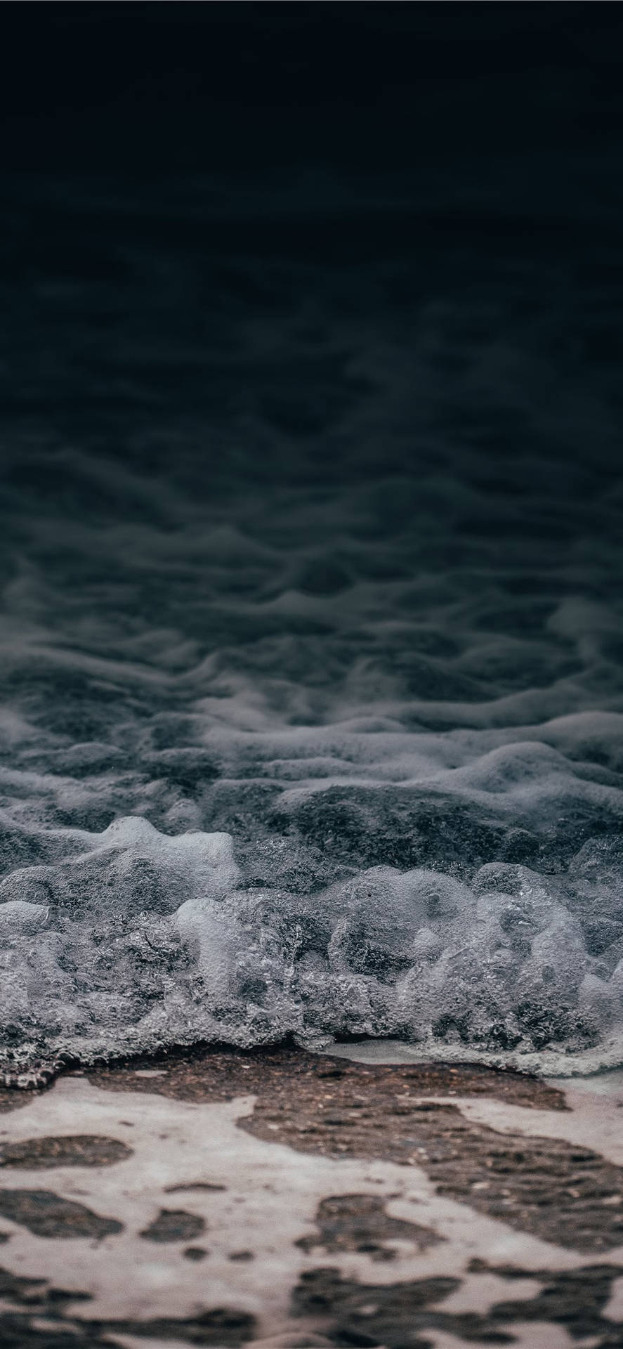 泡沫般的海浪在暮色中沖刷著黑暗的沙灘。 — iPhone X 壁紙