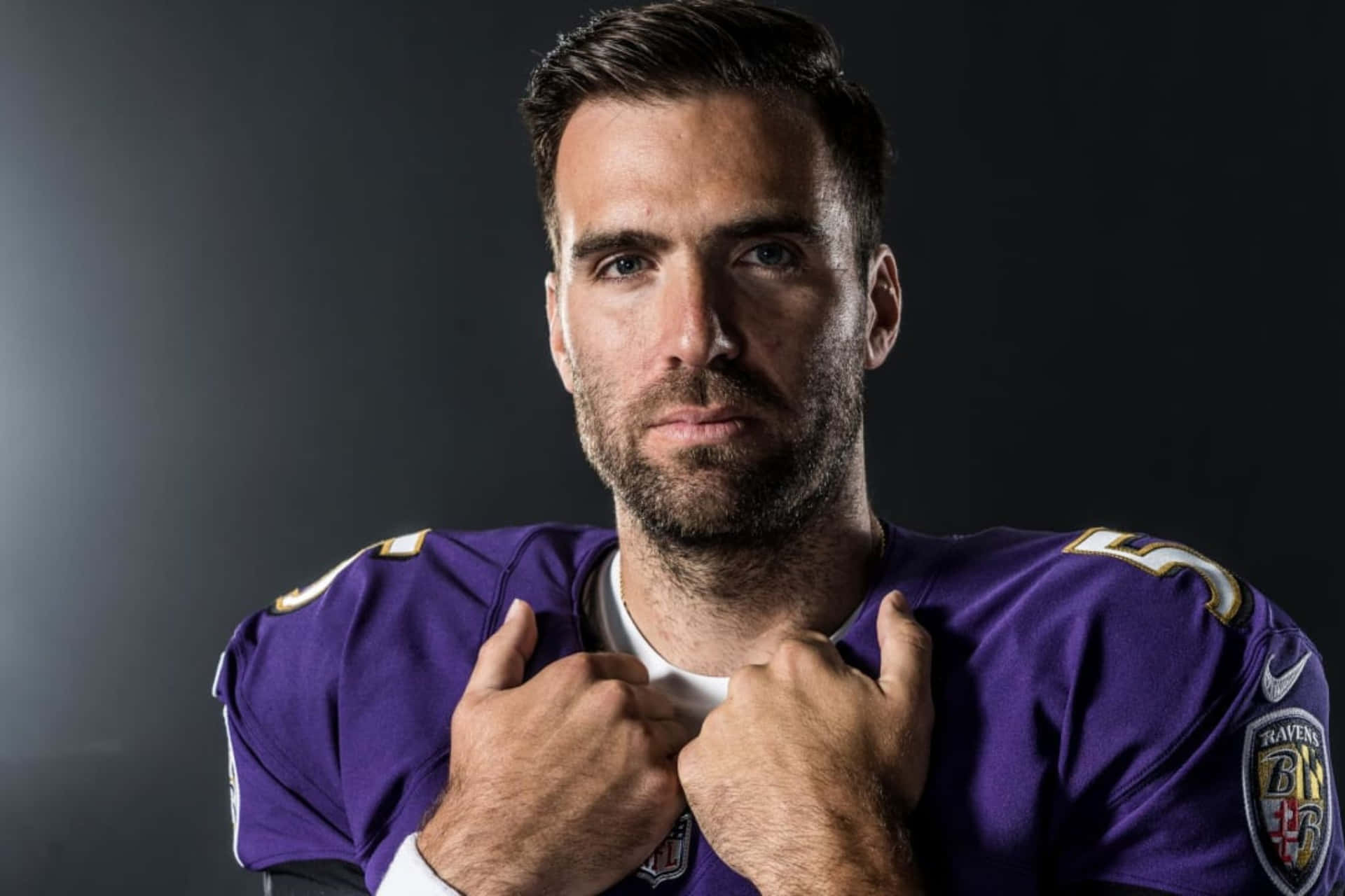  壁紙 — 一位專注的足球運動員身穿紫色Ravens球衣，在黑暗的攝影棚背景下抓住制服的領口。