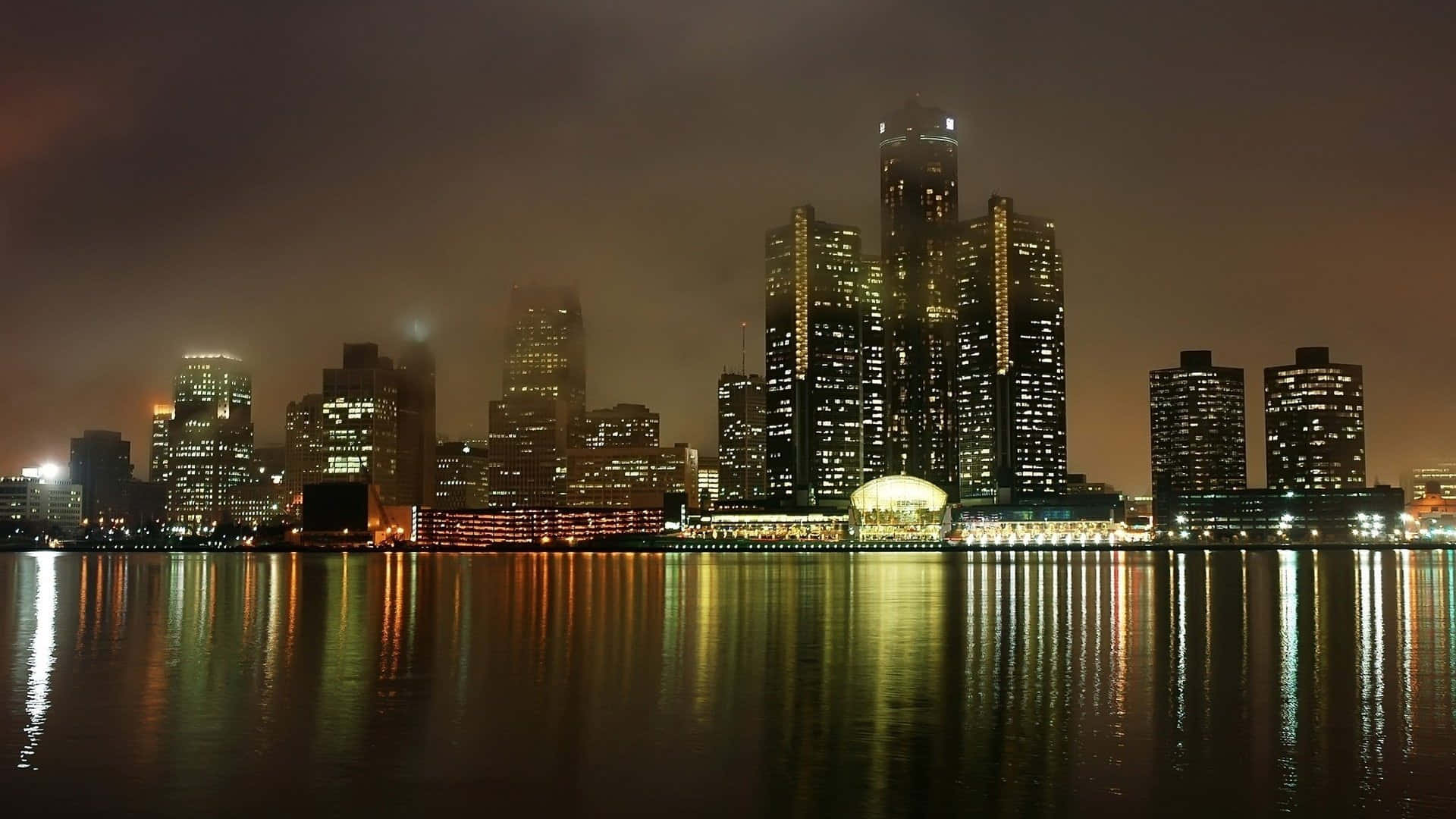 Windsor Canada 桌布 壁紙 — 霧夜城市景觀，高聳的摩天大樓在平靜的水面上反射出金色燈光。