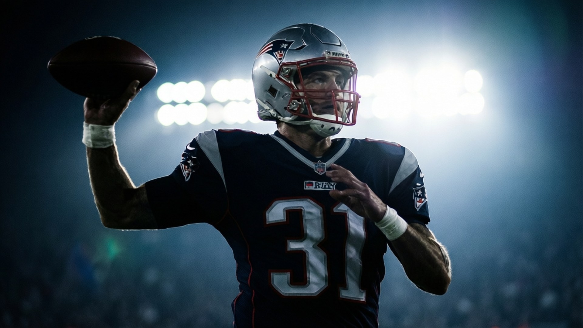 Tom Brady Silhouette 壁紙 — 一名身穿新英格蘭愛國者隊31號球衣的美式足球四分衛準備在體育場燈光下投球。