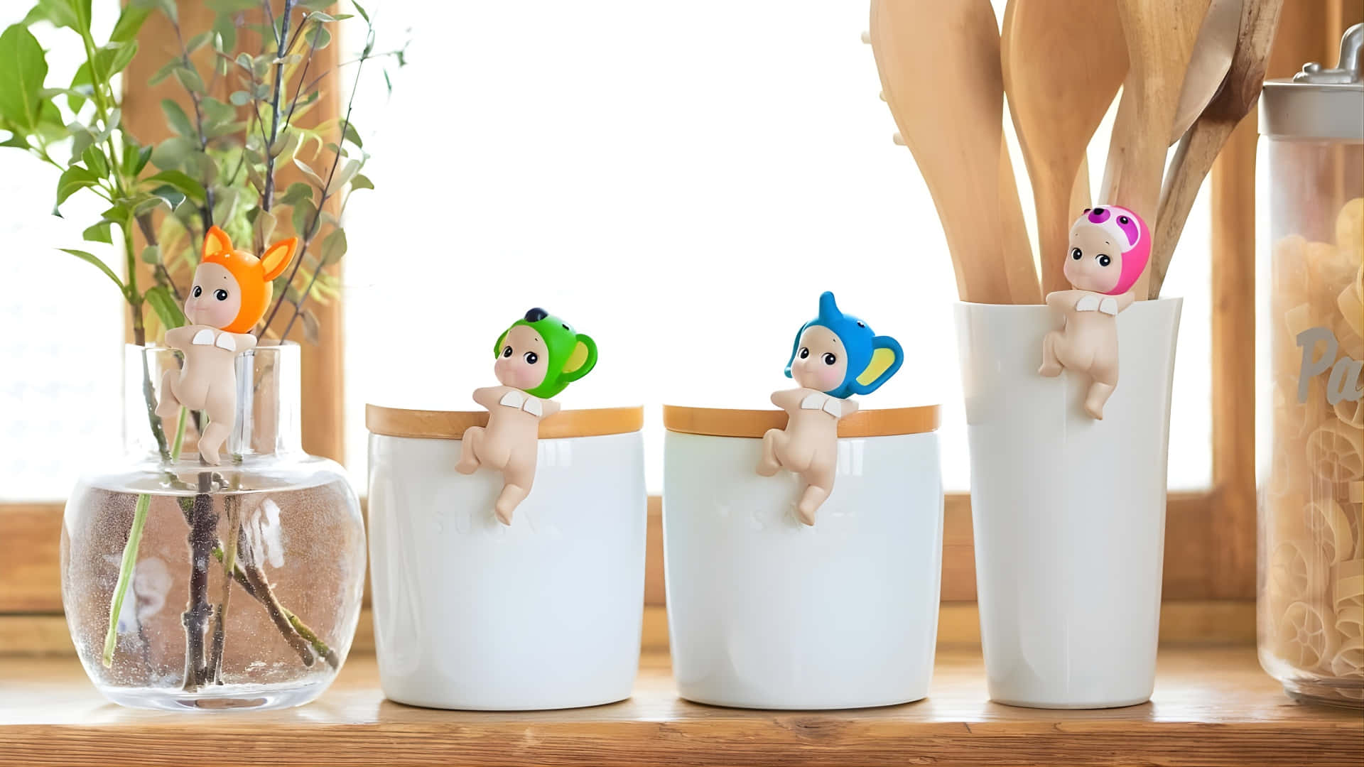  壁紙 — 四個戴動物帽的可愛公仔緊貼在木製檯面上的廚房容器上，旁邊有一盆植物和一個義大利麵罐。