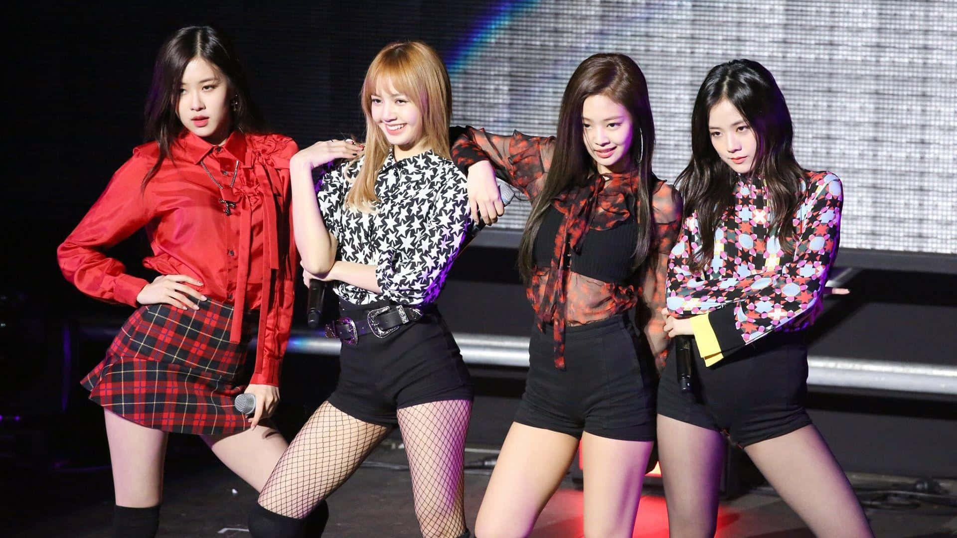 四位女K-pop表演者在燈光明亮的舞台上自信擺姿勢，穿著色彩繽紛的服裝。 — Blackpink 壁紙