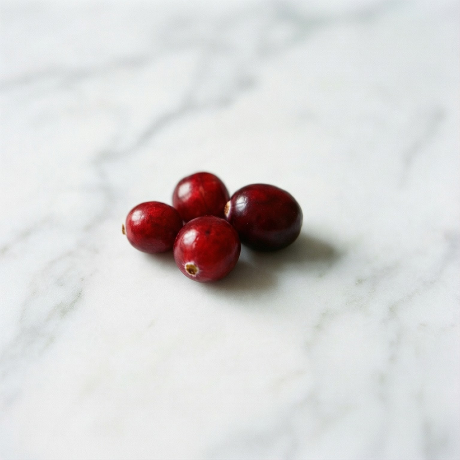 Cranberry Minimalist 壁紙 — 四顆光澤的紅色蔓越莓放在帶有灰色紋理的白色大理石表面上。