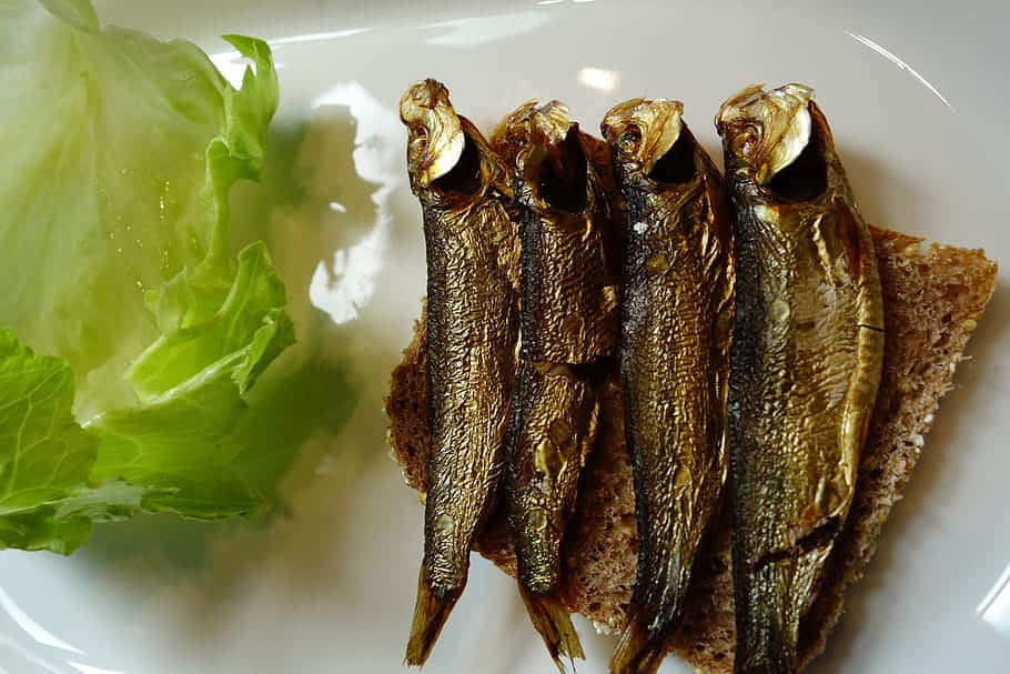  壁紙 — 四條金黃色煙燻魚排列在一片深色麵包上，旁邊是脆綠的生菜，放在白色盤子上。