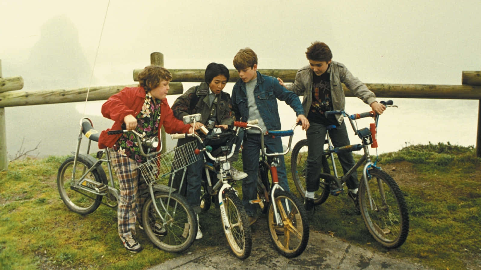  壁紙 — 四個穿著復古80年代服裝的小孩，帶著他們的BMX腳踏車，站在霧氣瀰漫的山坡上，俯瞰水面。