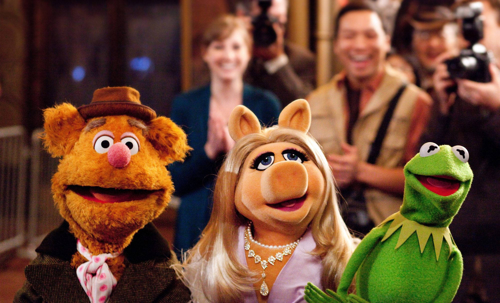 Fozzie Bear 桌布 壁紙 — Fozzie Bear、Miss Piggy 和 Kermit the Frog 對著鏡頭燦爛微笑，而攝影師在他們身後捕捉這個時刻。