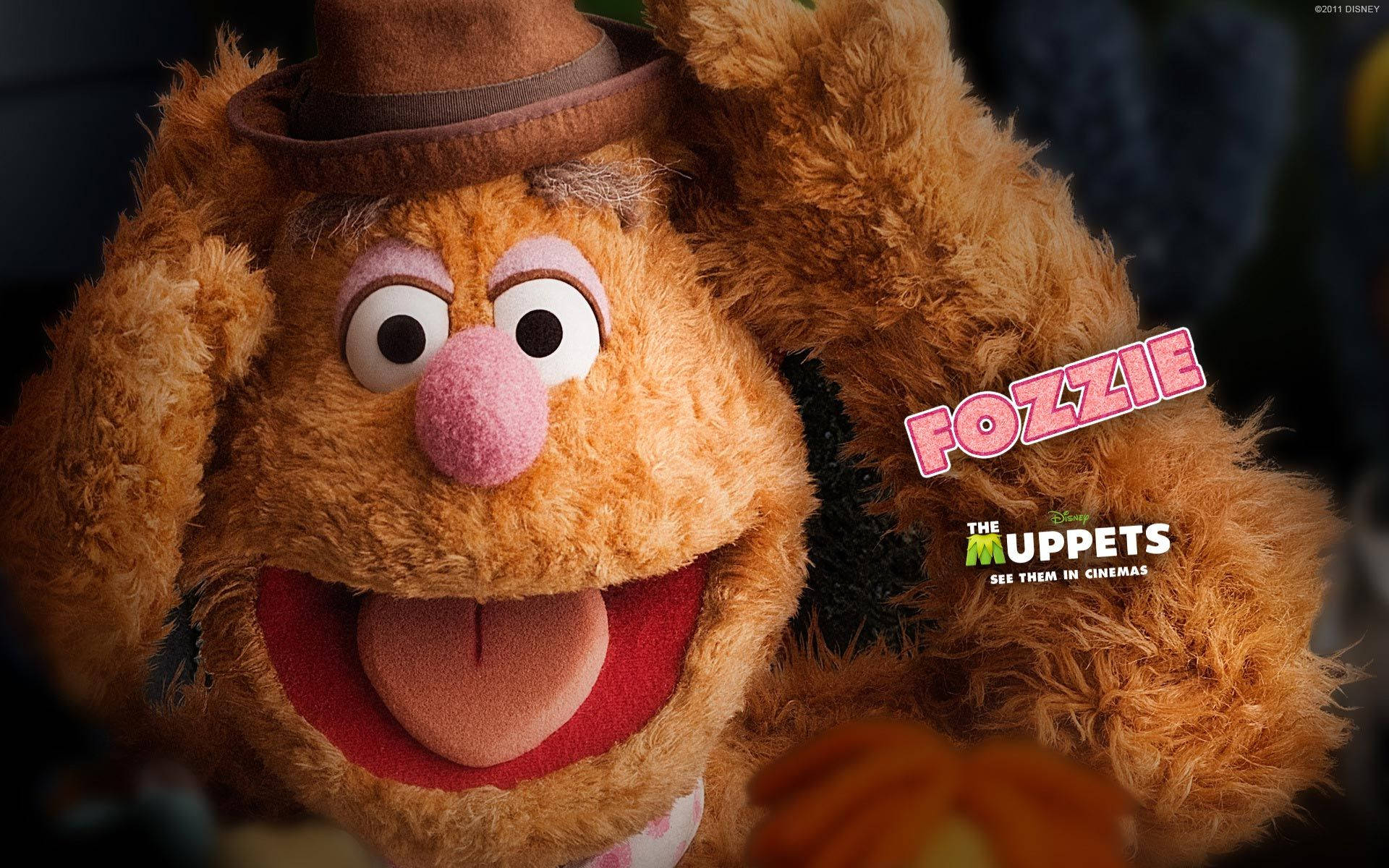 Fozzie Bear 桌布 壁紙 — Fozzie Bear 的特寫，戴著棕色 fedora 帽，咧嘴大笑，伸出舌頭，背景是深色。
