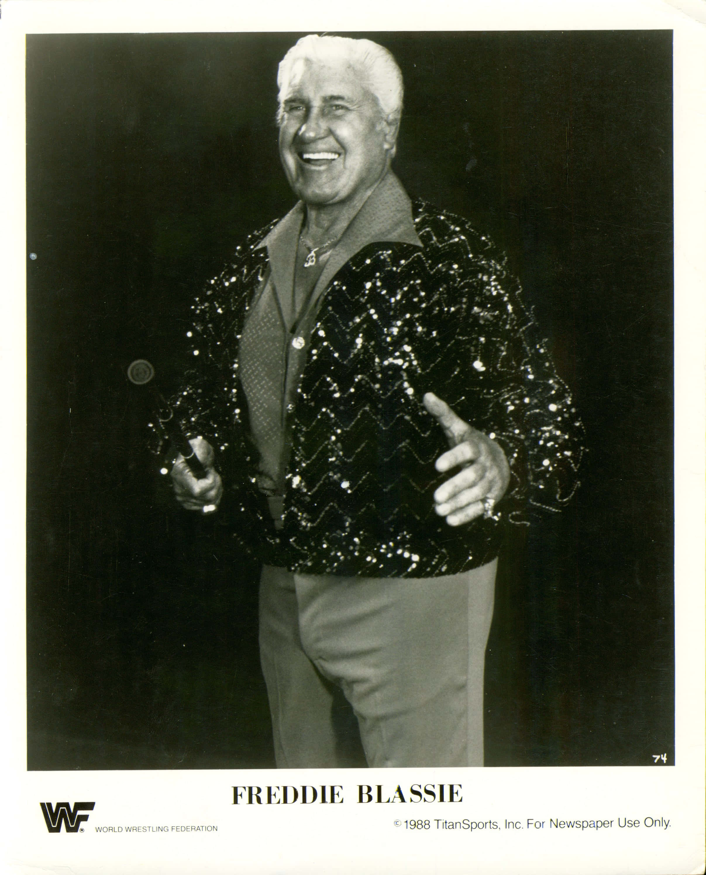 Smile 桌布 壁紙 — Freddie Blassie 身穿閃亮亮片外套，手持麥克風，在深色背景下咧嘴大笑。