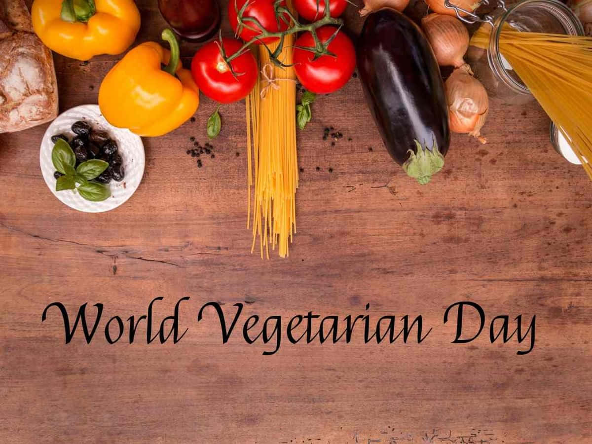  壁紙 — 新鮮蔬菜和義大利麵擺放在質樸的木桌上，帶有'World Vegetarian Day'文字。