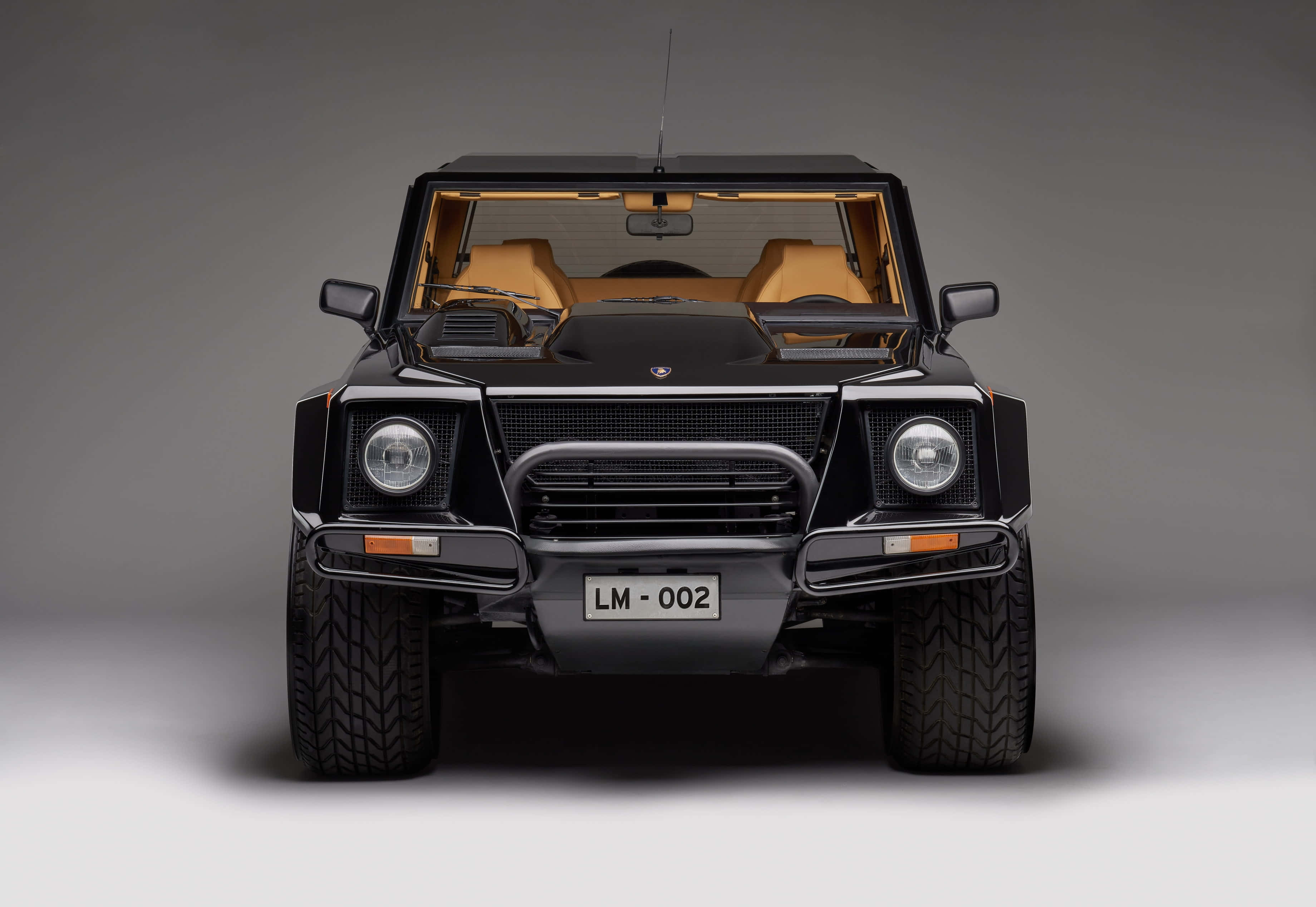 Lamborghini Lm002 桌布 壁紙 — 黑色藍寶堅尼LM002的正面視圖，配以棕褐色皮革座椅和鍍鉻裝飾，背景為中性灰色工作室背景。