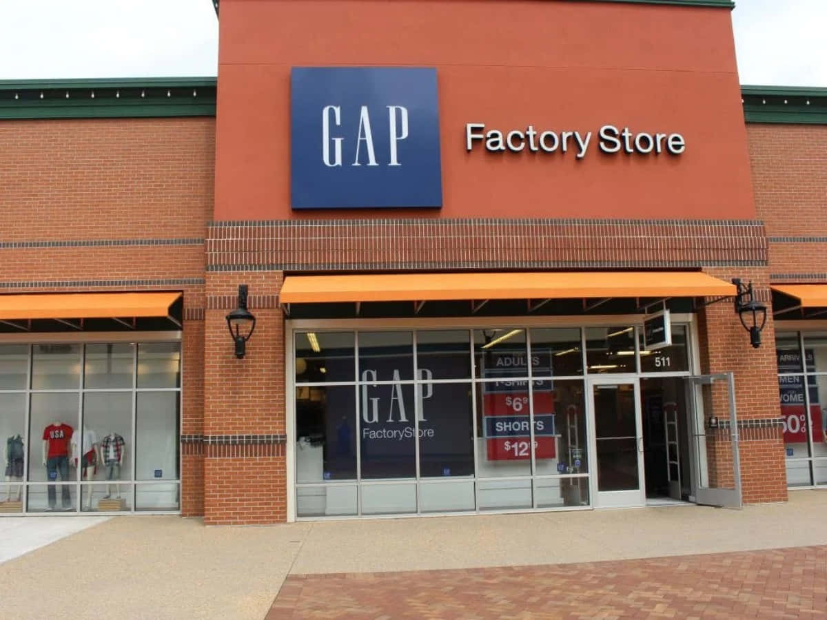 間隙 桌布 壁紙 — GAP Factory Store 正面外觀，磚砌外牆、橙色遮陽篷，窗戶上顯示特價標誌。