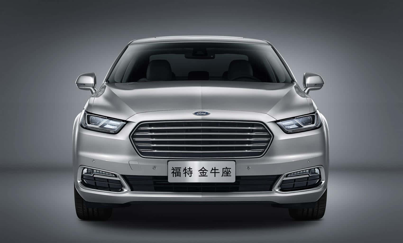 Ford Taurus 桌布 壁紙 — 銀色福特 Taurus 轎車正面視圖，配備現代化頭燈和進氣格柵，背景為漸變灰色工作室背景。